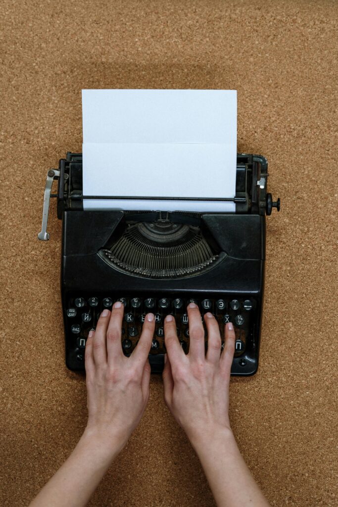 Hands typing on a vintage typewriter placed on a corkboard surface, creating a retro ambiance.